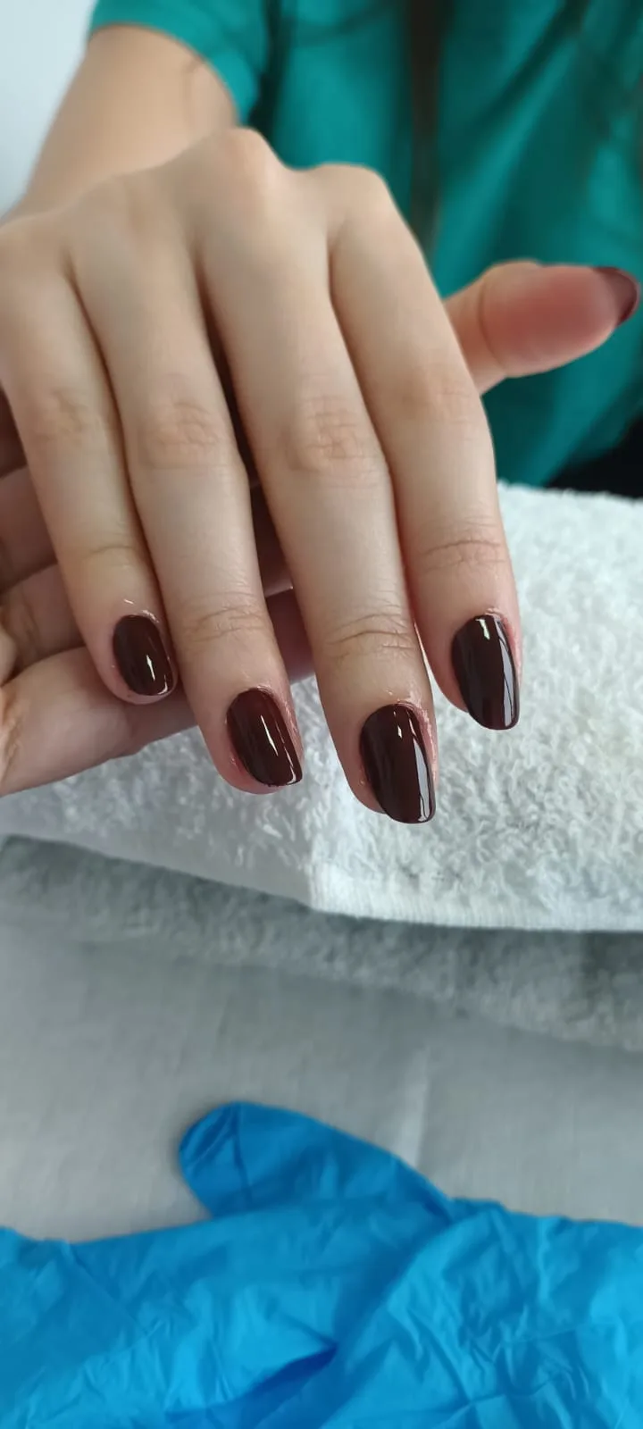 Unhas amendoadas com esmalte bordô, mão apoiada na toalha
