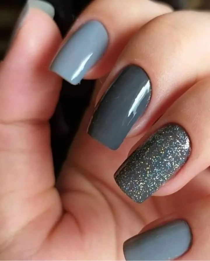 Unhas quadradas em tons de cinza, uma delas com glitter prateado