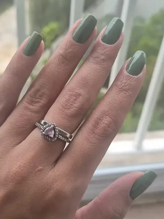 Unhas compridas com esmalte verde-oliva, mão com aliança na janela