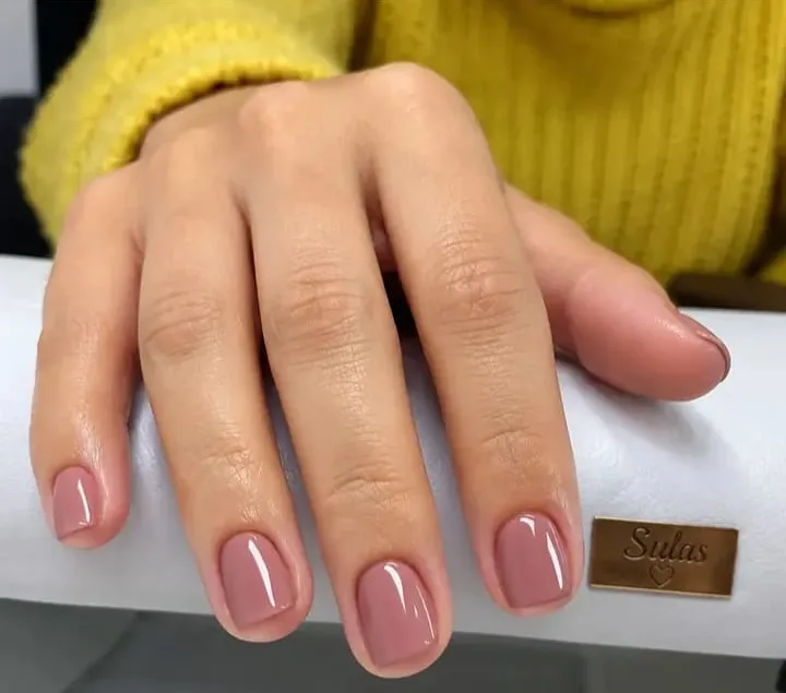 Unhas curtas com esmalte rosa antigo brilhante, mão apoiada em um apoio branco