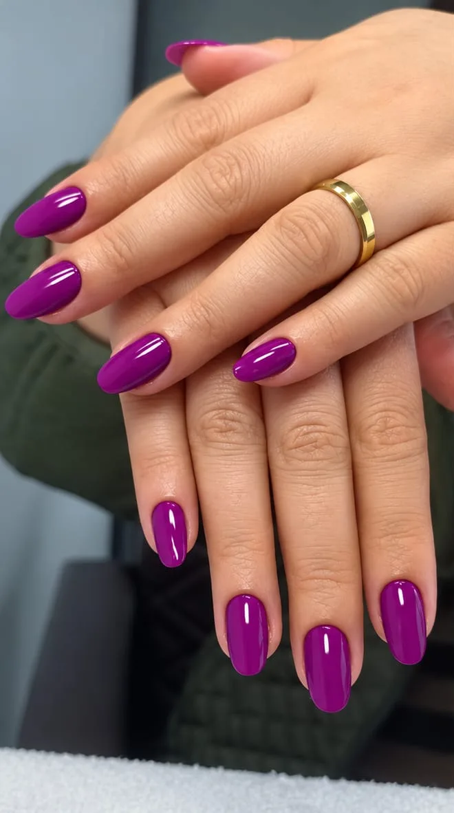 Unhas amendoadas com esmalte roxo vibrante, mãos sobrepostas, aliança dourada