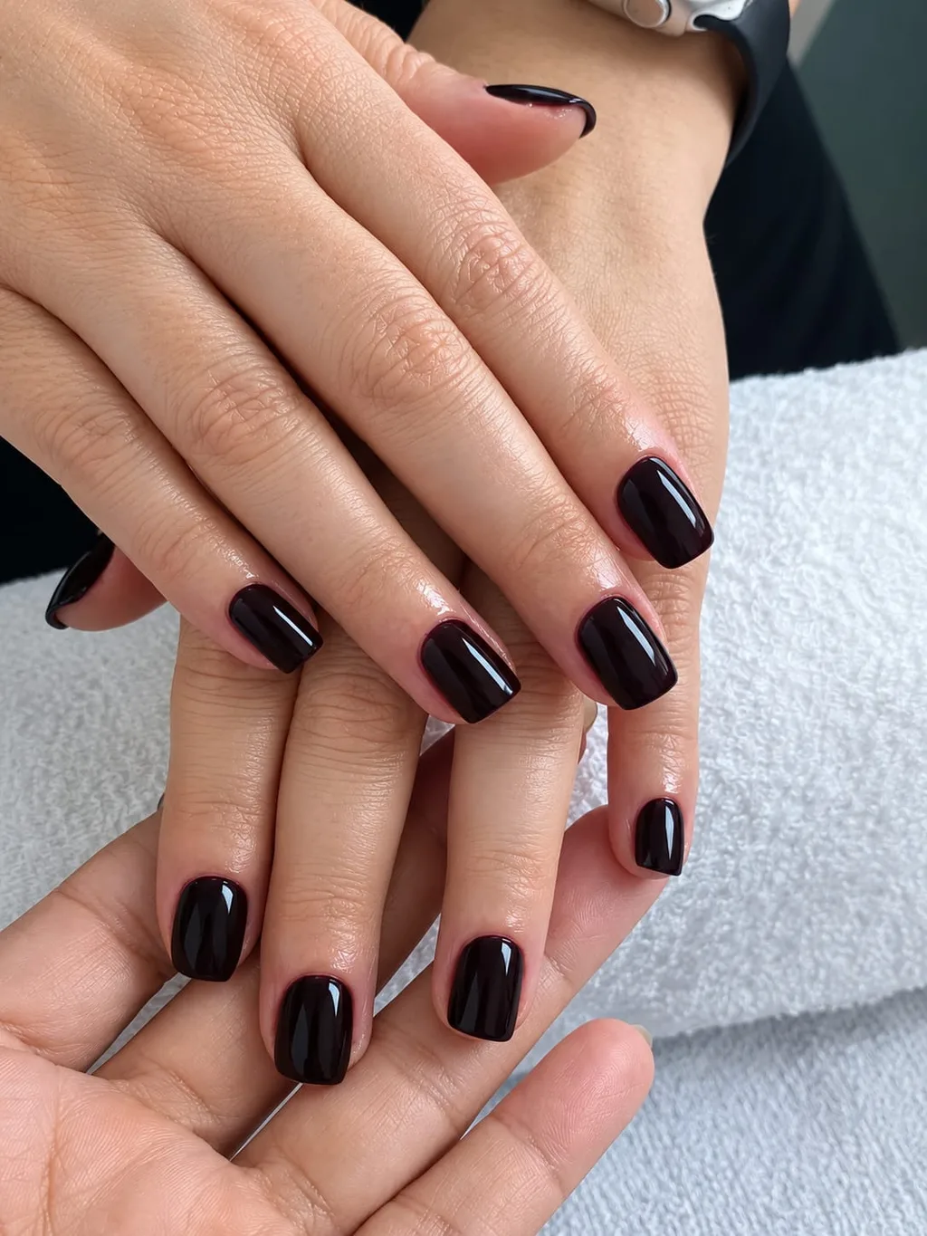 Unhas curtas com esmalte vinho escuro brilhante, mãos sobrepostas sobre toalha branca